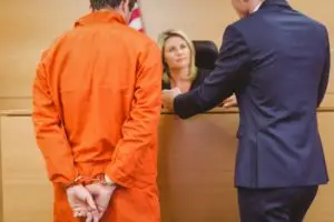 a man in handcuffs and his lawyer speaking with a judge