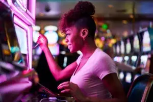 A woman in pink lighting pulls the handle of a casino slot machine.