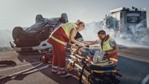 a person on a stretcher at a car crash site being attended to by emts