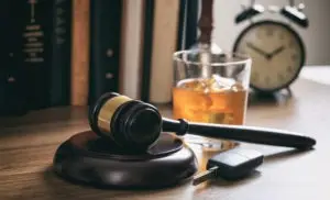 a car key a glass of alcohol and a gavel upon a desk