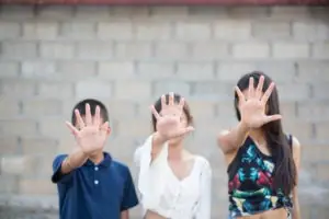 three children with hands out in front of their faces signing stop