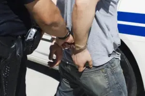 a handcuffed man being led to a police car by an officer