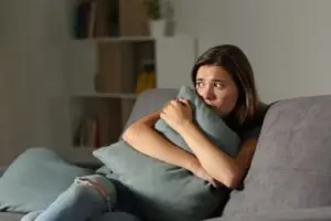 frightened woman hugging a pillow on her couch
