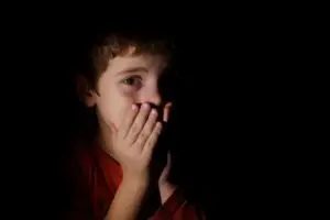 young boy in dark covering mouth with both hands