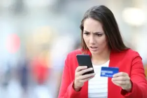 woman with credit card checking phone in disbelief