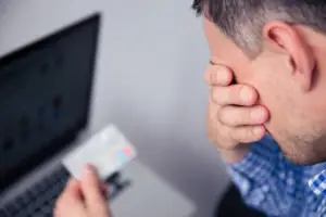 upset man holding a credit card by a laptop