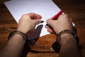 man in handcuffs signing confession document