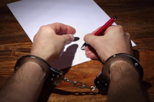 man in handcuffs signing confession document