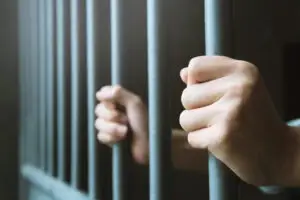 white hands holding prison bars