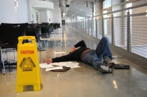 A man is lying on a wet floor with papers strewn around him after a slip-and-fall accident.