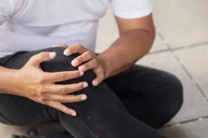 a man in a white t-shirt and black jeans holding his knee after a slip-and-fall accident