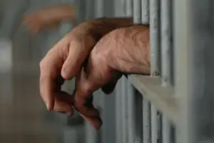 hands-of-a-man-convicted-of-possession-of-drugs-in-California-hanging-out-from-behind-the-bars-of-a-jail-cell