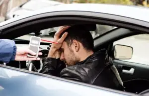 A man sits in a car while a police officer asks him to take a breathalyzer test. An excessive blood alcohol level is 0.15% or higher in California. A lawyer can help if you face a DUI charge.