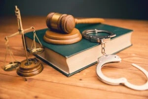 a gavel on a table next to a law book, handcuffs, and scales of justice. Types of sex crimes explained.