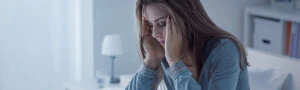 A distressed woman sitting on a bed, holding her head in her hands