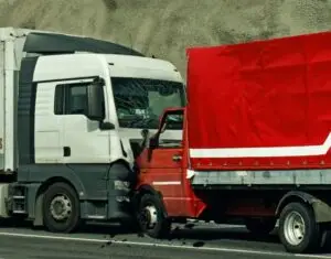 A collision between two trucks on the road, with the cabin of a white truck crashing into the rear of a red truck