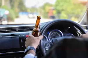 A man holds a beer bottle while driving