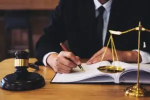 A lawyer in a suit, writing in a book, next to a gavel and scales.