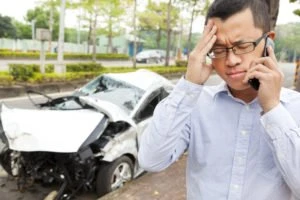 A man on a cell phone next to a wrecked car.