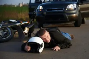 A motorcyclist lies on the road after an accident with a car.