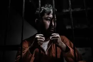 A man is sad while holding onto prison bars.