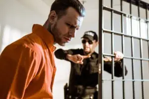 A sad man being lead into a jail cell by a guard.