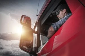 A truck driver sits in a red commercial truck.