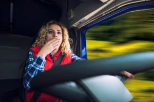 A truck driver yawns while driving her truck.