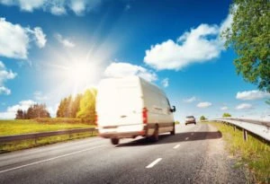 A white delivery van driving on a highway.