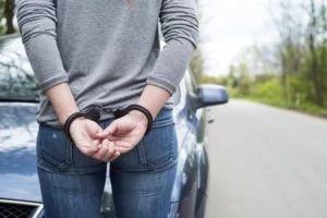 A woman is arrested by her car.