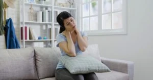 A woman on a couch, rubbing her shoulders.