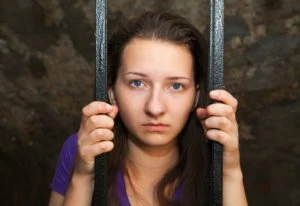 A young woman behind prison bars.