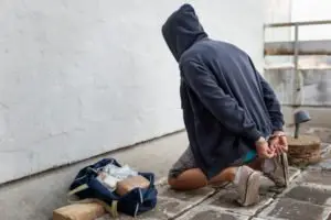 An arrested man kneeling near a bag of drugs.