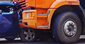 Blue car crushed by a large orange truck.