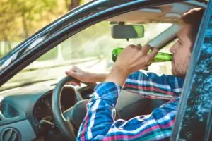 A man drinking from a beer bottle while driving.
