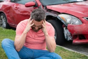 A man holding his head near his damaged red car.