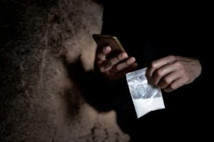 A man holding a phone and a bag of drugs.