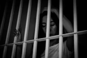 A sad woman behind prison bars.