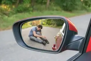 A side-view mirror view of an injured man on a road.
