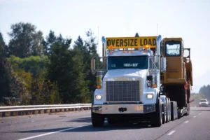 A truck with an oversize load banner carrying construction equipment.