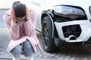 An upset woman crouching near her damaged car.