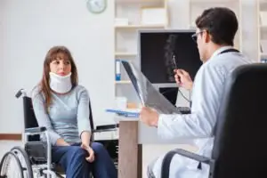 A woman in a wheelchair and neck brace talks with her doctor.