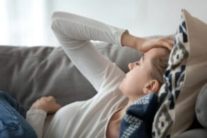 A woman laying on her couch, holding her head.