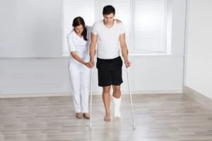 A young man on crutches is helped by a physiotherapist.