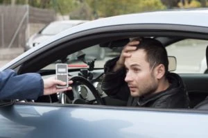 A cop showing a driver a breathalyzer.