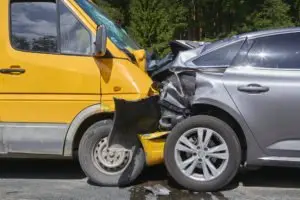 A crash between a yellow delivery van and a gray car.