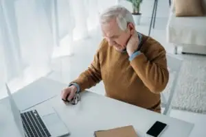 An older man at his desk, rubbing his neck.