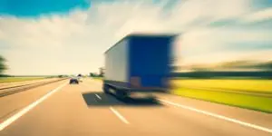 A blue truck speeds up to cars on a highway.