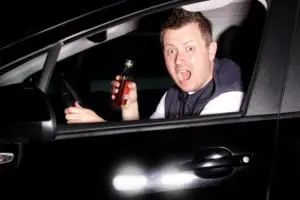 A driver holding alcohol looks panicked at oncoming traffic.