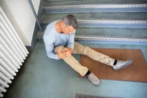 A man sitting on the floor, holding his knee, after falling down stairs.